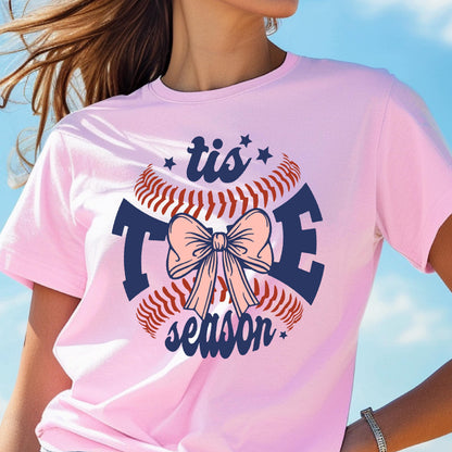May include: Pink t-shirt with a baseball graphic and the text "tis the season" in navy blue. The baseball has a pink bow on it.