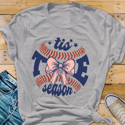 May include: Gray t-shirt with a baseball graphic and the text "tis the season" in blue and red. A pink bow is in the center of the baseball.
