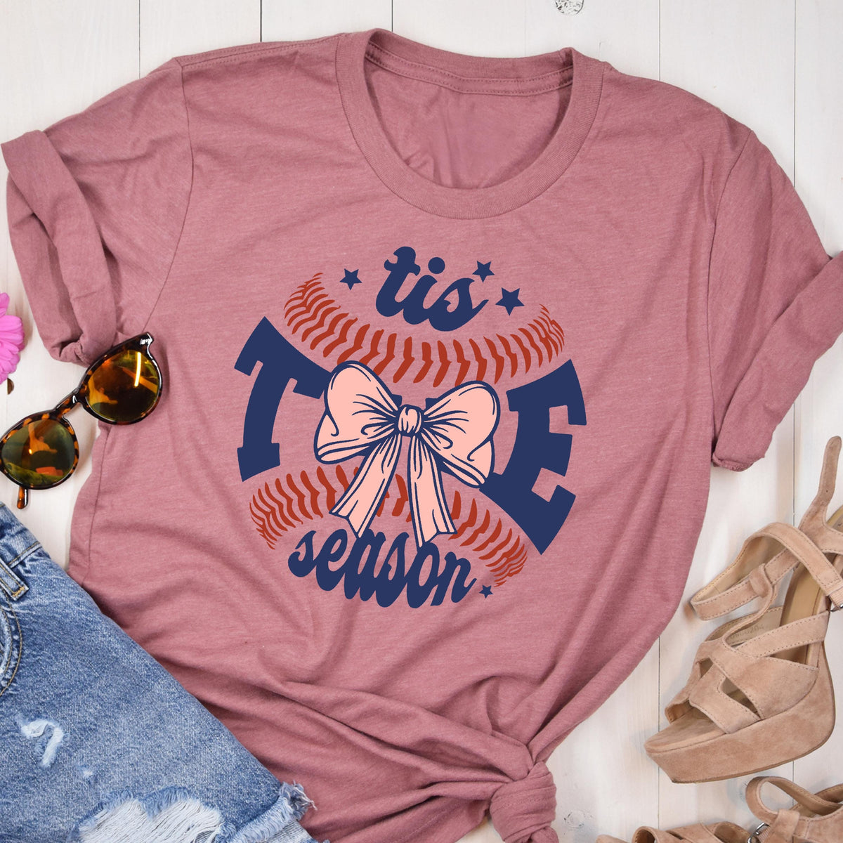 May include: A pink heather t-shirt with a baseball graphic and the text "tis the season" in navy blue. A pink bow is in the center of the baseball graphic.