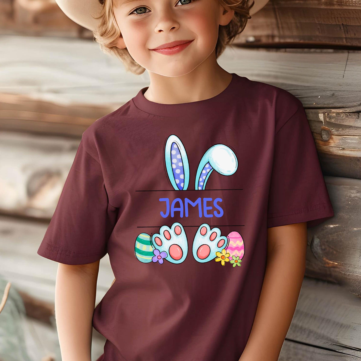 May include: Burgundy t-shirt with a cartoon bunny rabbit design. The bunny has blue ears with white polka dots and blue feet with pink paw pads. The shirt has the name "JAMES" printed on it.