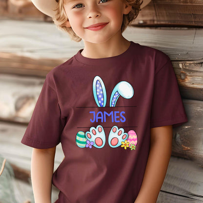 May include: Burgundy t-shirt with a cartoon bunny rabbit design. The bunny has blue ears with white polka dots and blue feet with pink paw pads. The shirt has the name "JAMES" printed on it.