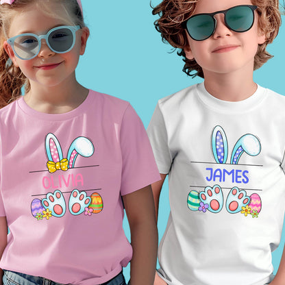 May include: Two children's t-shirts with Easter bunny ears and paw prints. The pink shirt has the name "Olivia" on it and the white shirt has the name "JAMES" on it.
