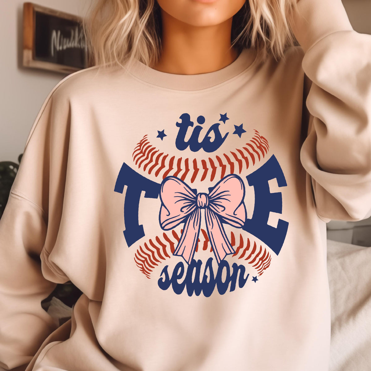 May include: A beige sweatshirt with a baseball graphic and the text "tis the season" in blue. The baseball graphic has a pink bow in the center.