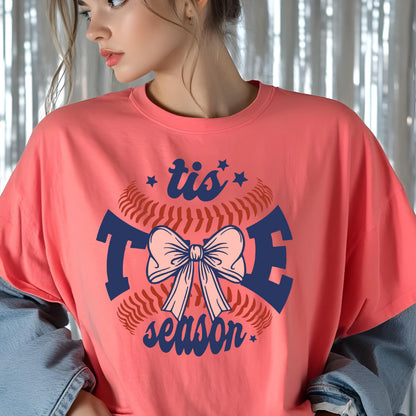 May include: A pink t-shirt with a baseball graphic and the text "tis the season" in navy blue. The baseball graphic features a pink bow.
