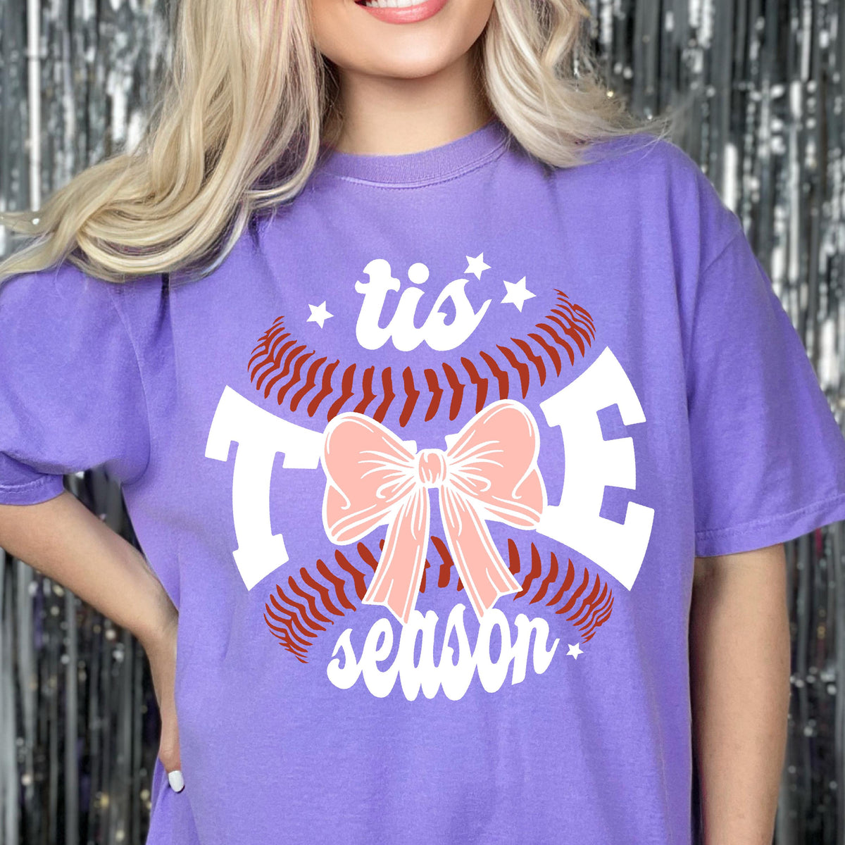 May include: Purple t-shirt with a white baseball graphic and the text "tis the season" with a pink bow.