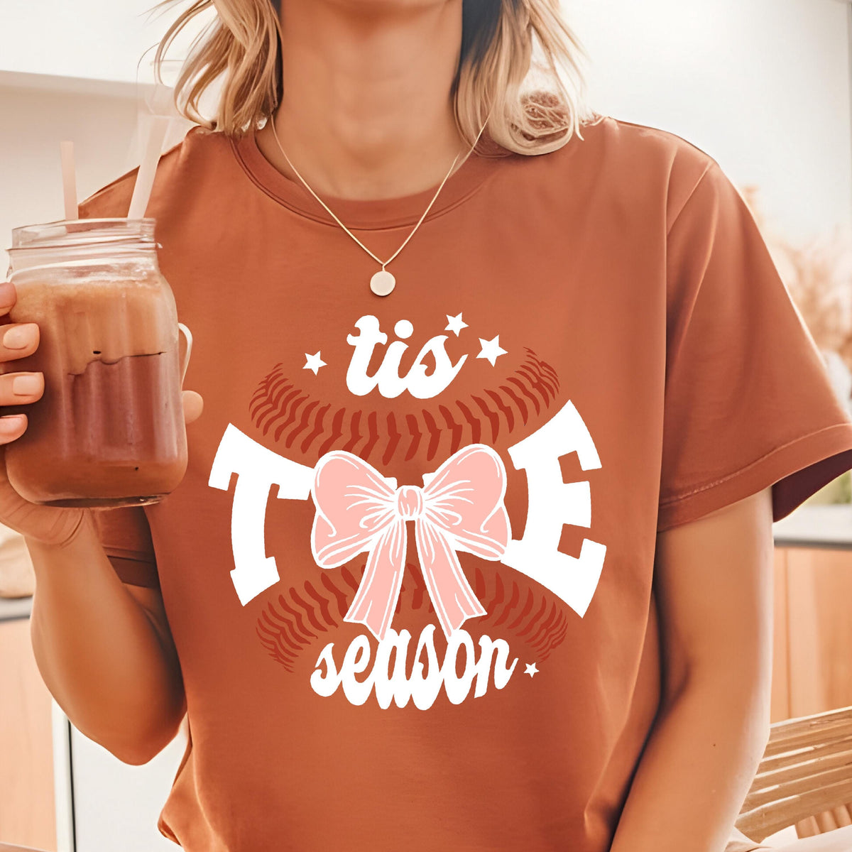 May include: A brown t-shirt with a white baseball graphic and the text "tis the season" with a pink bow in the center.