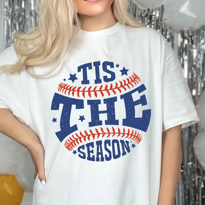 May include: White t-shirt with a blue and red baseball graphic and the text "Tis the Season" printed on it.