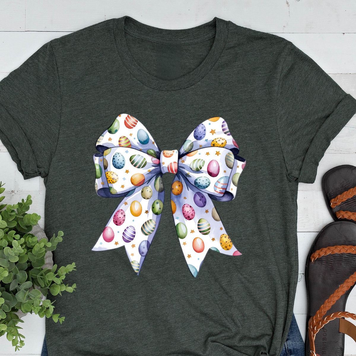May include: A dark green t-shirt with a white bow printed on the front. The bow is decorated with colorful Easter eggs.