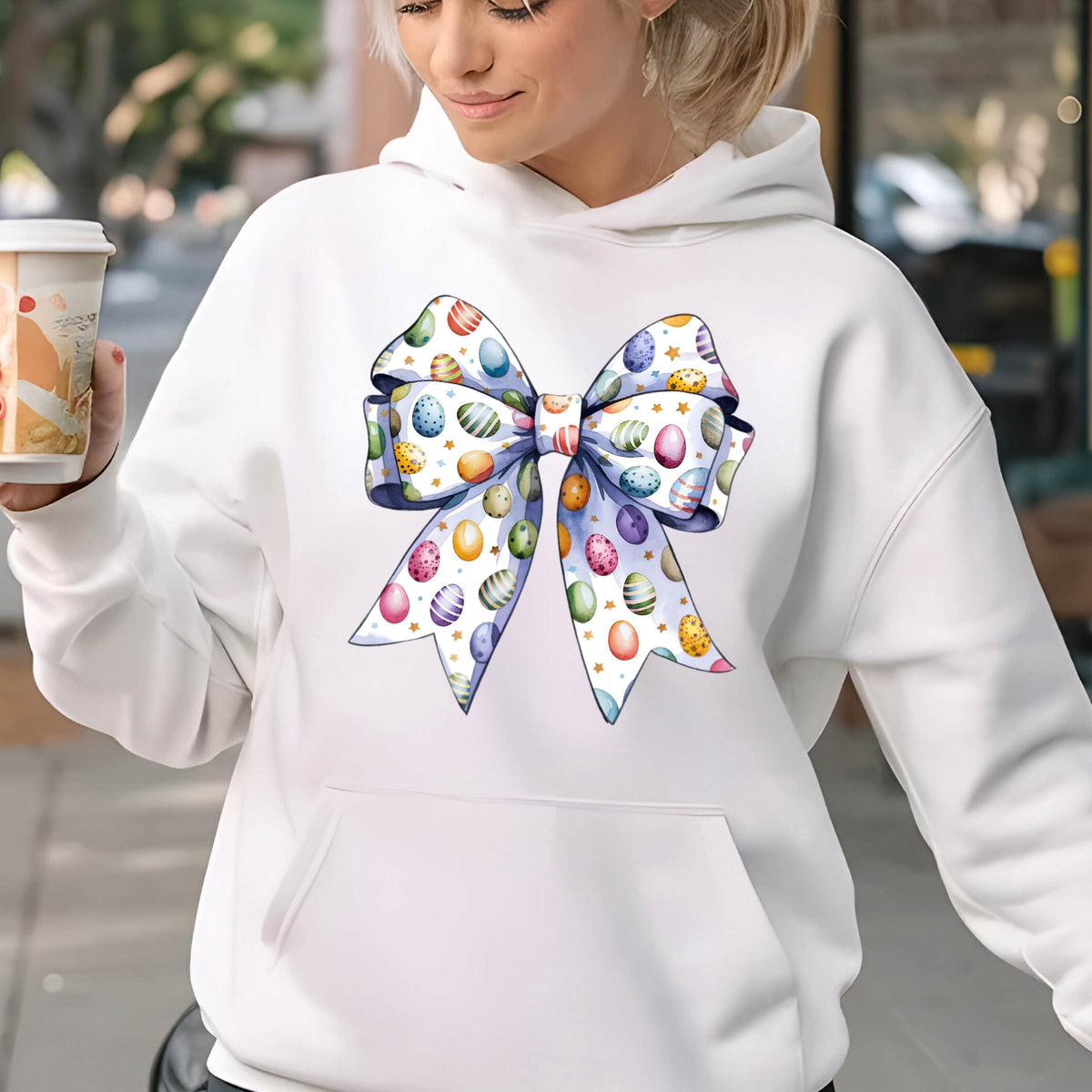 May include: White hoodie with a large blue and white bow printed on the front. The bow is decorated with colorful Easter eggs.