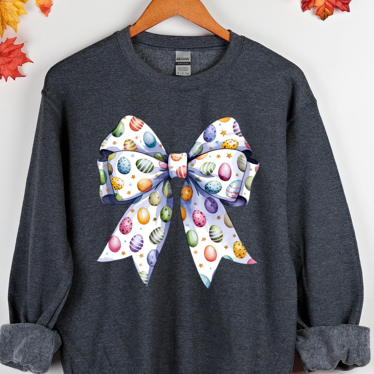 May include: A dark gray sweatshirt with a white bow printed on the front. The bow is decorated with colorful Easter eggs.