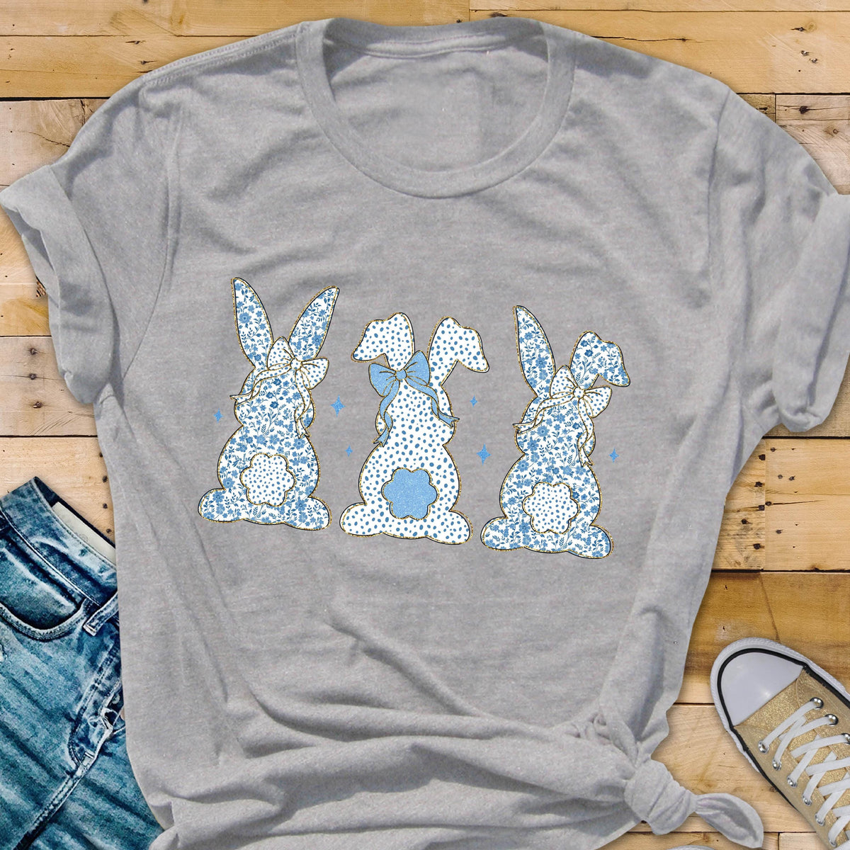 May include: A gray t-shirt with a design of three blue and white patterned bunnies with bows. The bunnies are facing away from the viewer.