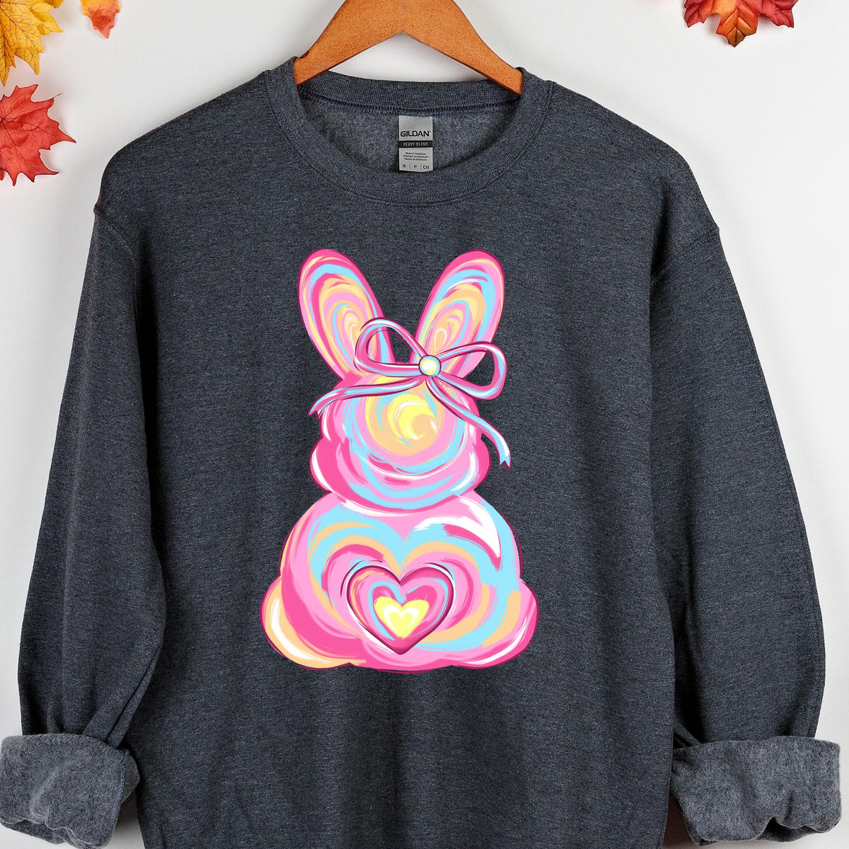 May include: A dark gray sweatshirt with a colorful Easter bunny design. The bunny is pink, blue, yellow, and orange with a pink bow. The bunny has a heart in the center of its body.
