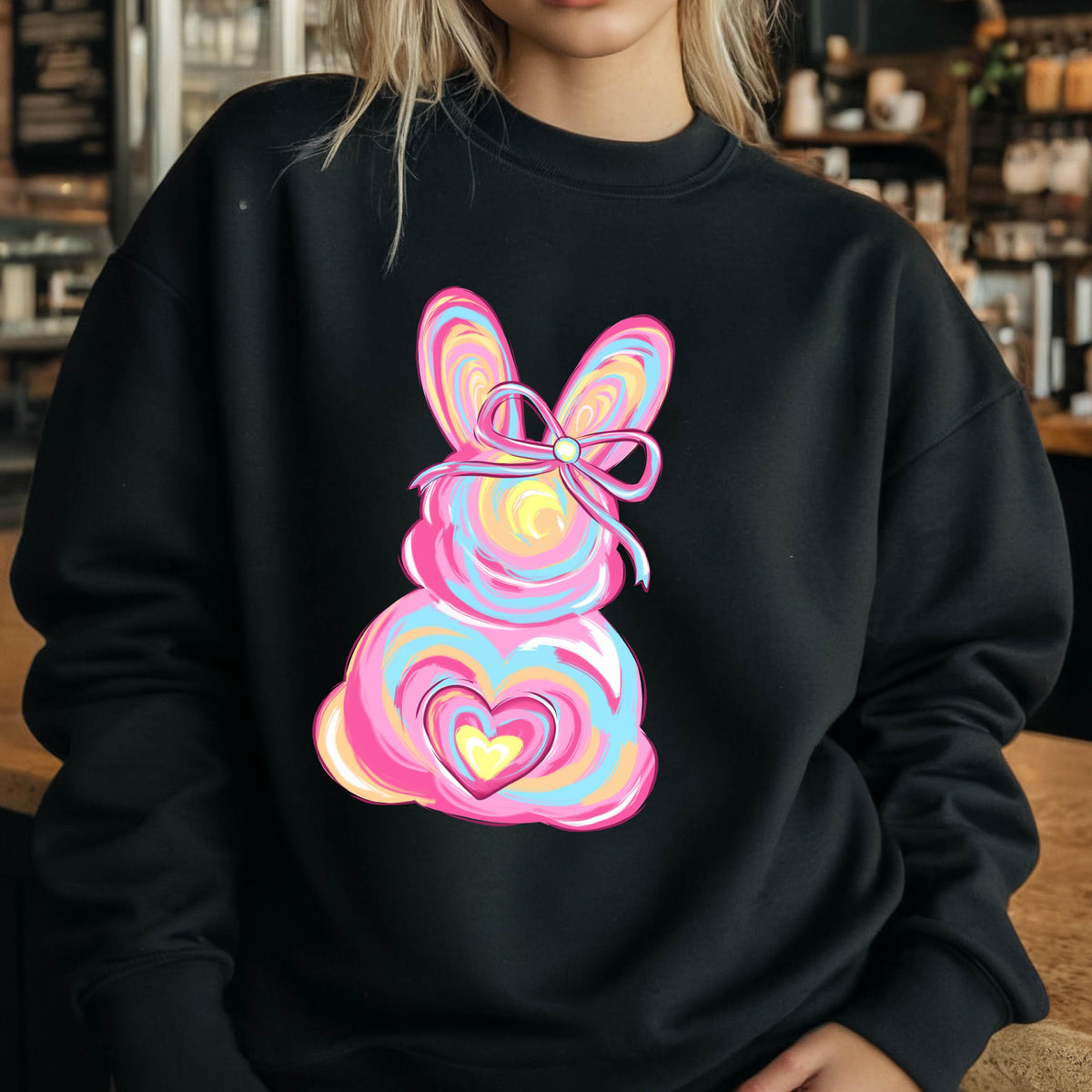 May include: Black sweatshirt with a colorful abstract bunny design. The bunny has a pink, blue, and yellow swirl pattern and a pink bow with a pearl in the center.
