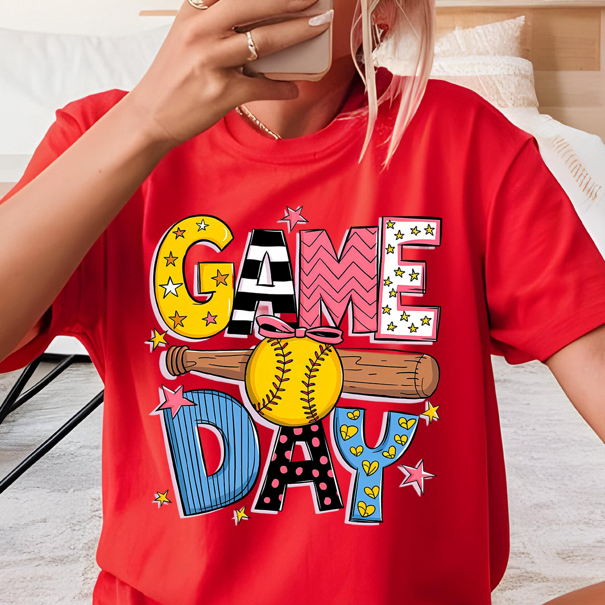 May include: Red t-shirt with a colorful graphic design that says "GAME DAY" with a baseball and bat. The letters are decorated with stars, polka dots, and hearts.