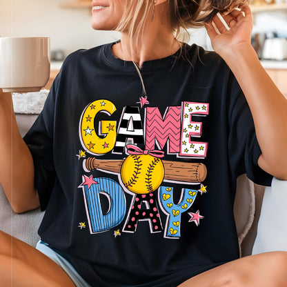 May include: Black t-shirt with a colorful graphic design that says "GAME DAY" with a softball and bat. The graphic has stars, hearts, and zig-zag patterns.