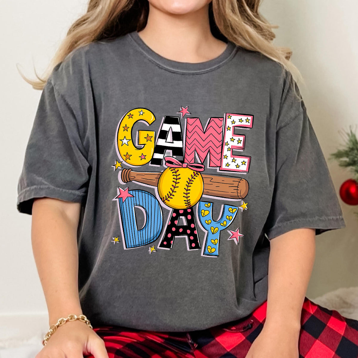 May include: A gray t-shirt with a colorful graphic design that says "GAME DAY" with a baseball and bat. The graphic is in a cartoon style with stars, stripes, polka dots, and hearts.