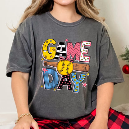 May include: A gray t-shirt with a colorful graphic design that says "GAME DAY" with a baseball and bat. The graphic is in a cartoon style with stars, stripes, polka dots, and hearts.