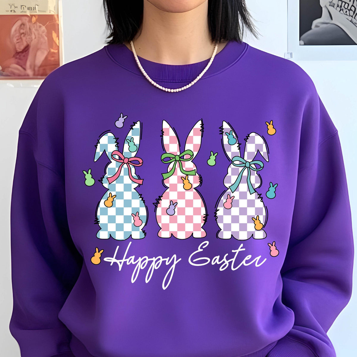 May include: Purple sweatshirt with a graphic of three pastel checkered Easter bunnies and the text "Happy Easter".