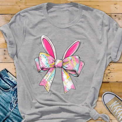 May include: A gray t-shirt with a pink and white bow with bunny ears. The bow has a colorful, abstract pattern.