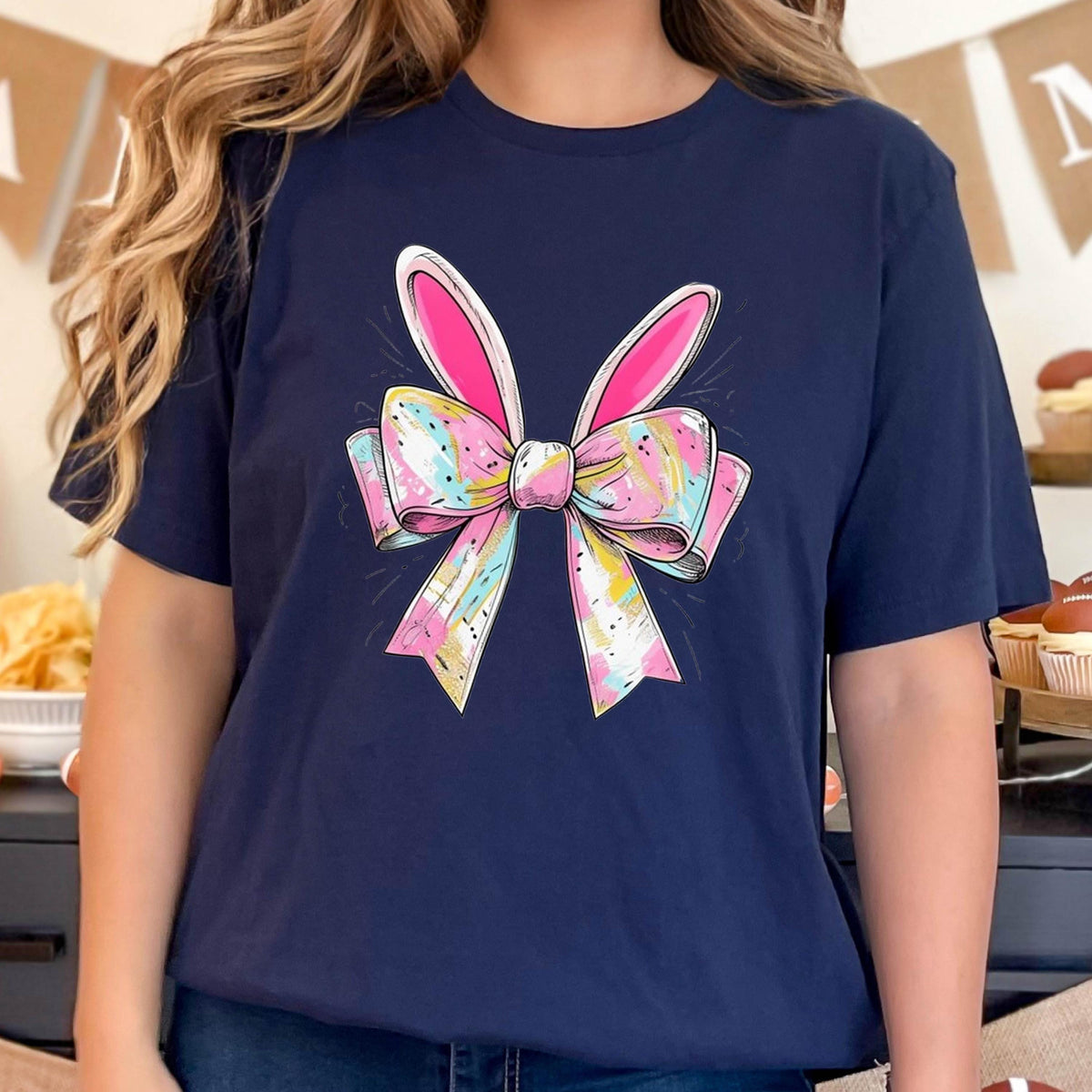 May include: A navy blue t-shirt with a colorful bow and bunny ears design. The bow is pink, yellow, blue, and white. The bunny ears are pink.