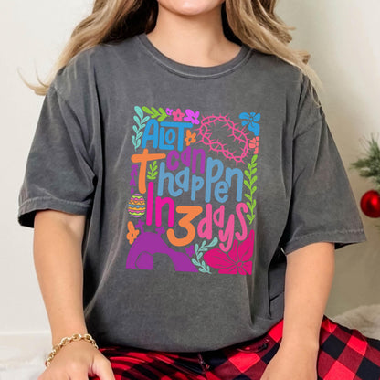 May include: A gray t-shirt with a colorful graphic design that says "A lot can happen in 3 days". The graphic includes flowers, leaves, and an Easter egg.