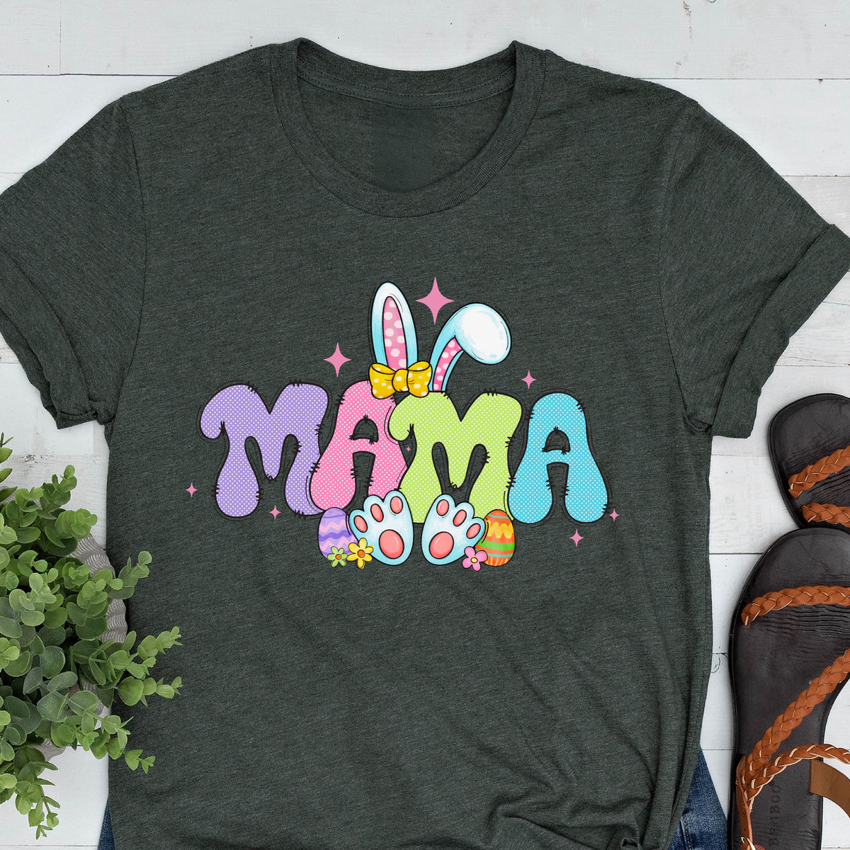 May include: A dark green t-shirt with a colorful Easter bunny design and the word "MAMA" in a playful font. The bunny is wearing a pink bow and holding colorful Easter eggs.