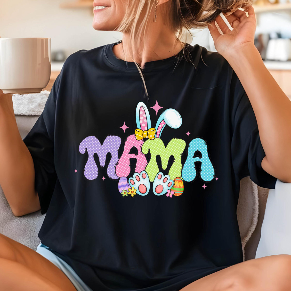 May include: Black t-shirt with the word "MAMA" in pastel colors, decorated with bunny ears, a yellow bow, and Easter eggs. The design is perfect for Easter or Mother's Day.