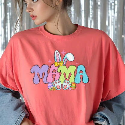 May include: Coral-colored t-shirt with the word "MAMA" in a colorful, cartoonish font. The design includes bunny ears, a bow, Easter eggs, and bunny feet, perfect for Easter or Mother's Day.