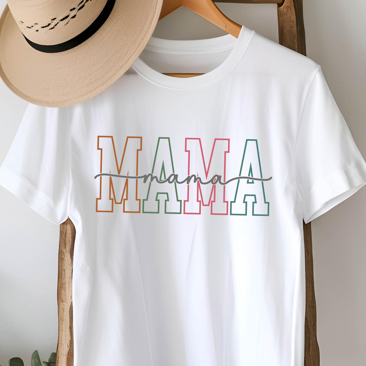 May include: White t-shirt with the word "MAMA" in colorful block letters with a handwritten "mama" underneath.