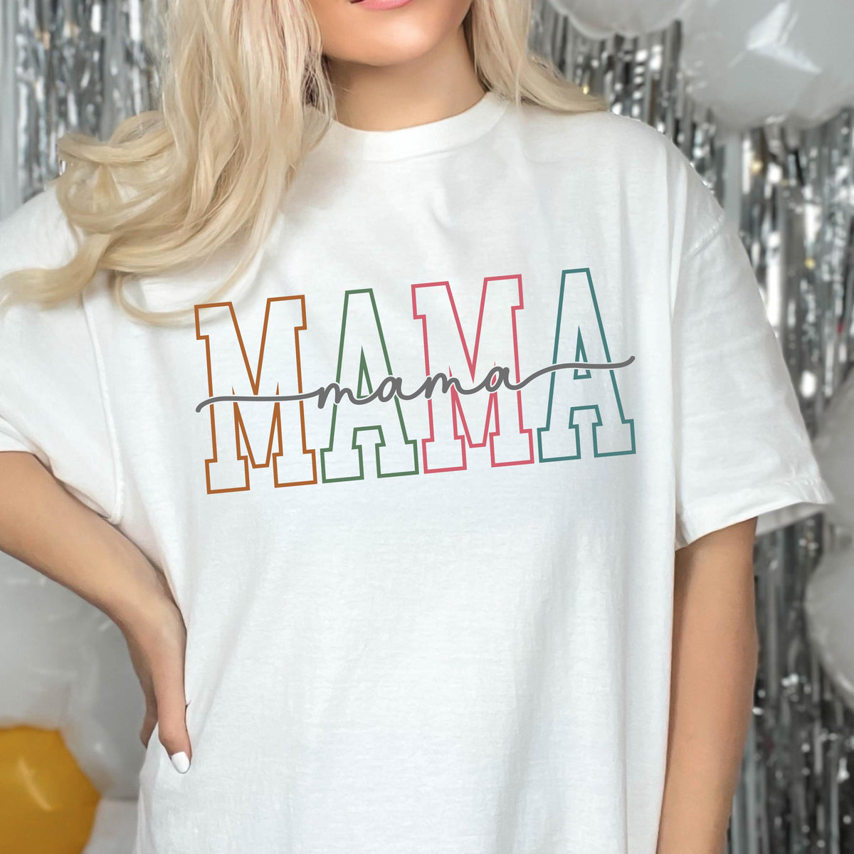 May include: White t-shirt with the word "MAMA" in colorful block letters and the word "mama" written in cursive underneath.