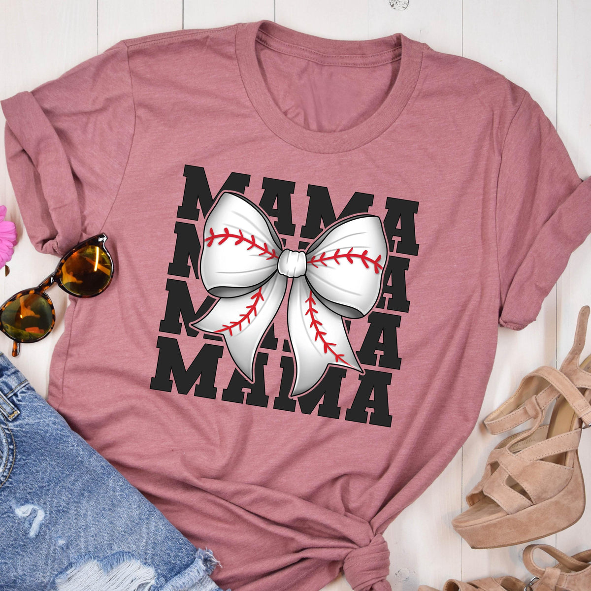 May include: A pink t-shirt with a black graphic of the word "MAMA" repeated four times. A white baseball-themed bow is centered on the graphic.