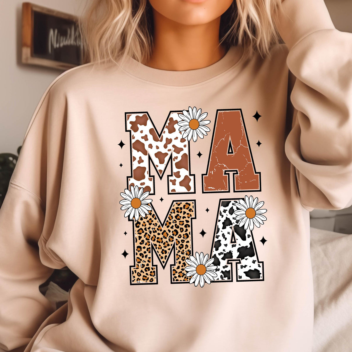 May include: A tan sweatshirt with the word "MAMA" printed on the front. The letters are decorated with cow print, leopard print, and brown fabric. Each letter has a white daisy flower next to it.