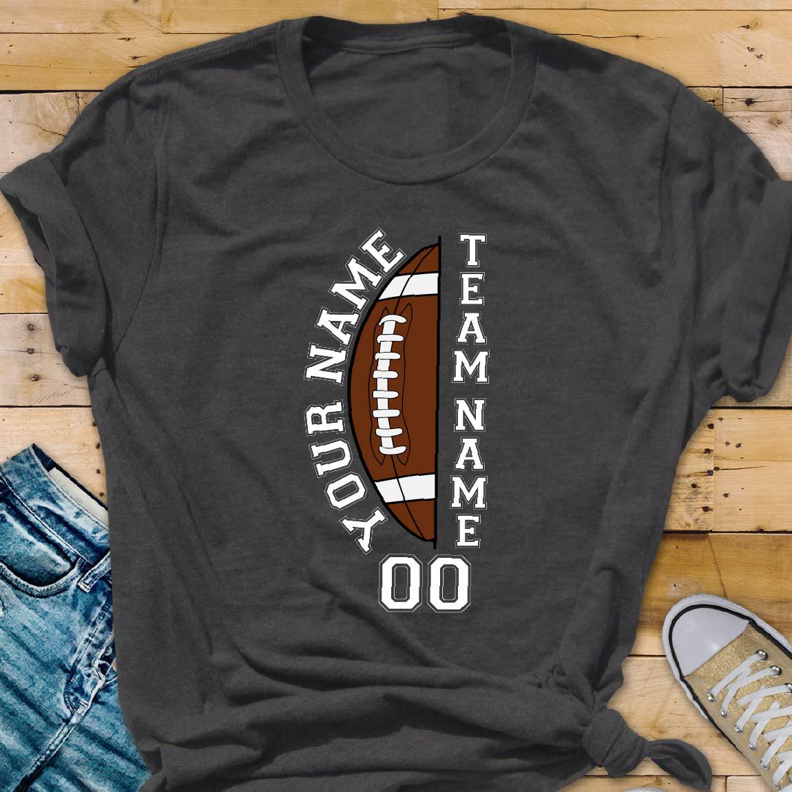 May include: A dark gray short-sleeve t-shirt featuring a graphic of a brown football split in half. The text YOUR NAME is printed vertically on the left, TEAM NAME on the right, and the number 00 is printed in white below the football graphic.