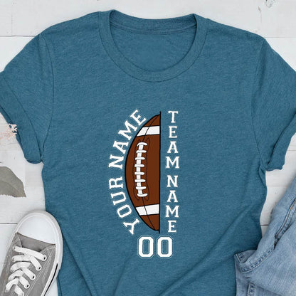 May include: A heathered teal crew neck t-shirt featuring a graphic of a brown football split in half. The text "YOUR NAME" is printed vertically on the left, "TEAM NAME" on the right, and the number "00" is centered below the football graphic.