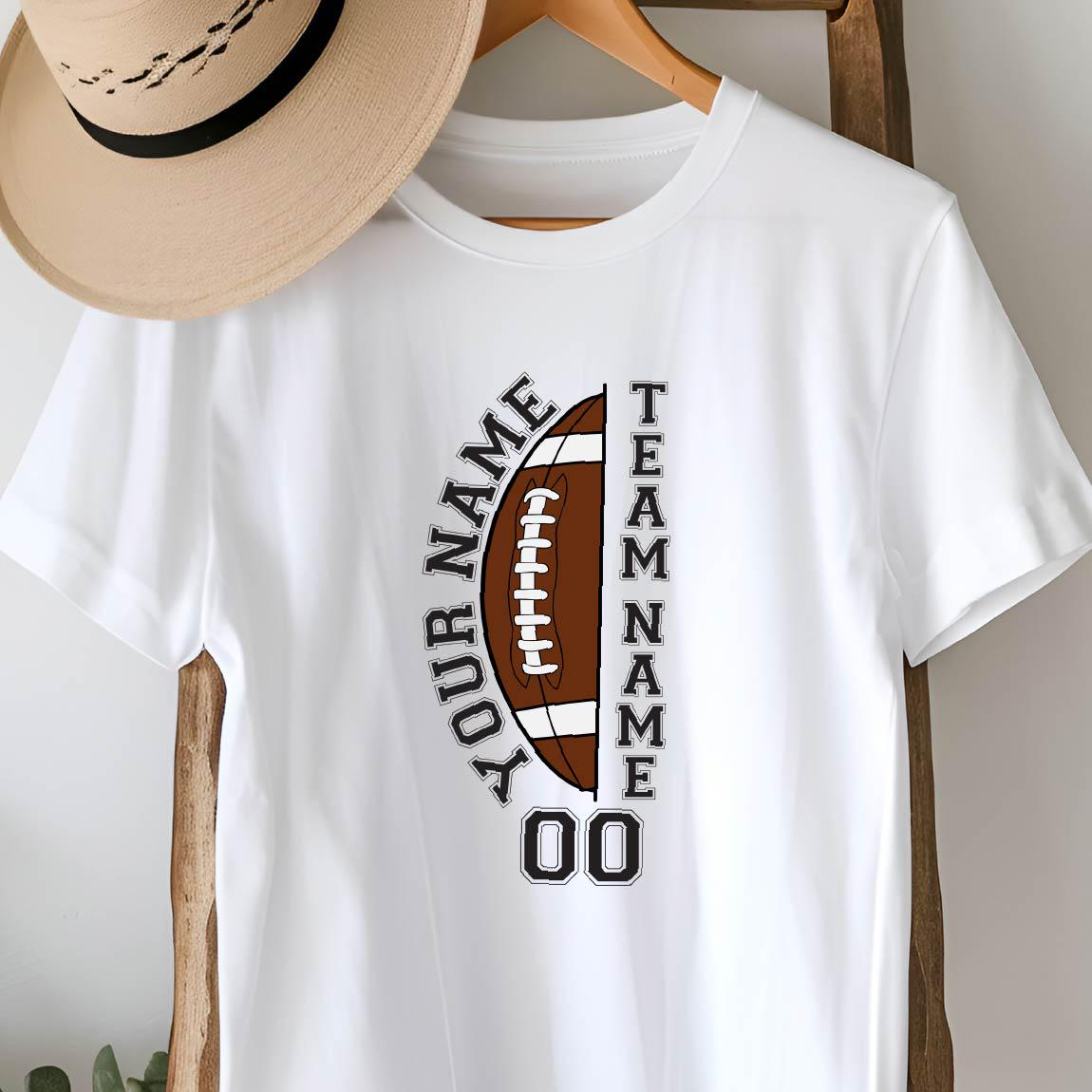 May include: A white short-sleeved t-shirt featuring a graphic of a brown football split vertically. The text "YOUR NAME" is arched on the left, "TEAM NAME" is vertical on the right, and "00" is printed below. A tan fedora hat rests above the shirt.