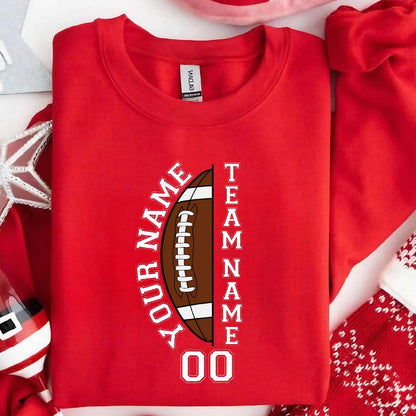 May include: A red sweatshirt with a football graphic. The football is brown and white, with the words "YOUR NAME" and "TEAM NAME" in white. The number "00" is below the football.