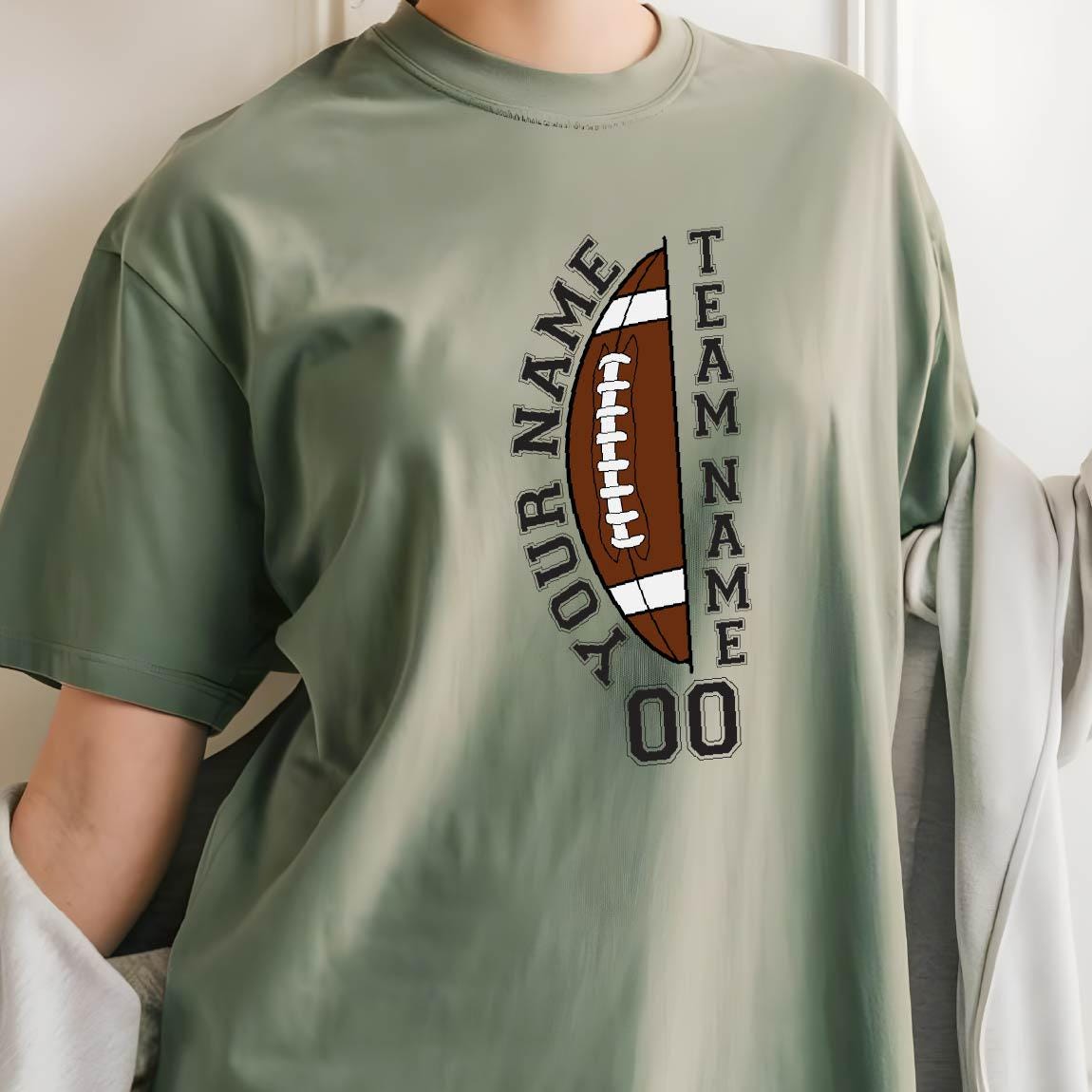 May include: Sage green t-shirt featuring a brown football graphic with white laces. The design includes the text "YOUR NAME" and "TEAM NAME" in black, along with the number "00".