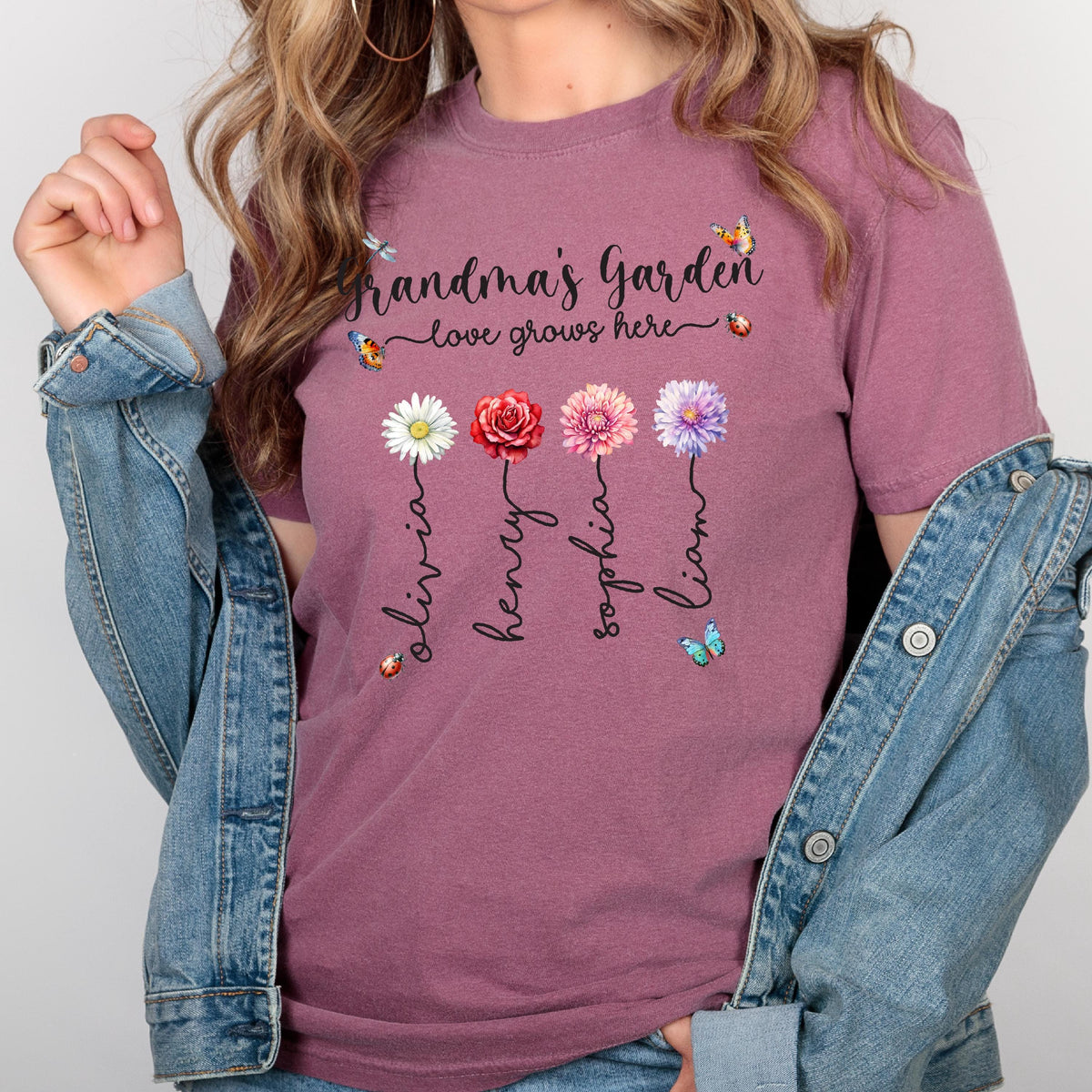 May include: A mauve t-shirt with the text "Grandma's Garden - love grows here" and four flowers with names Olivia, Henry, Sophia, and Liam written underneath each flower.