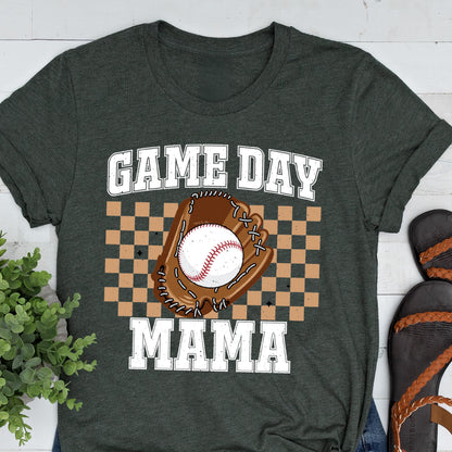 May include: A dark charcoal gray t-shirt featuring a graphic print with the text GAME DAY MAMA in white block letters. The center design includes a brown baseball glove holding a white baseball, set against a tan and brown checkered background.