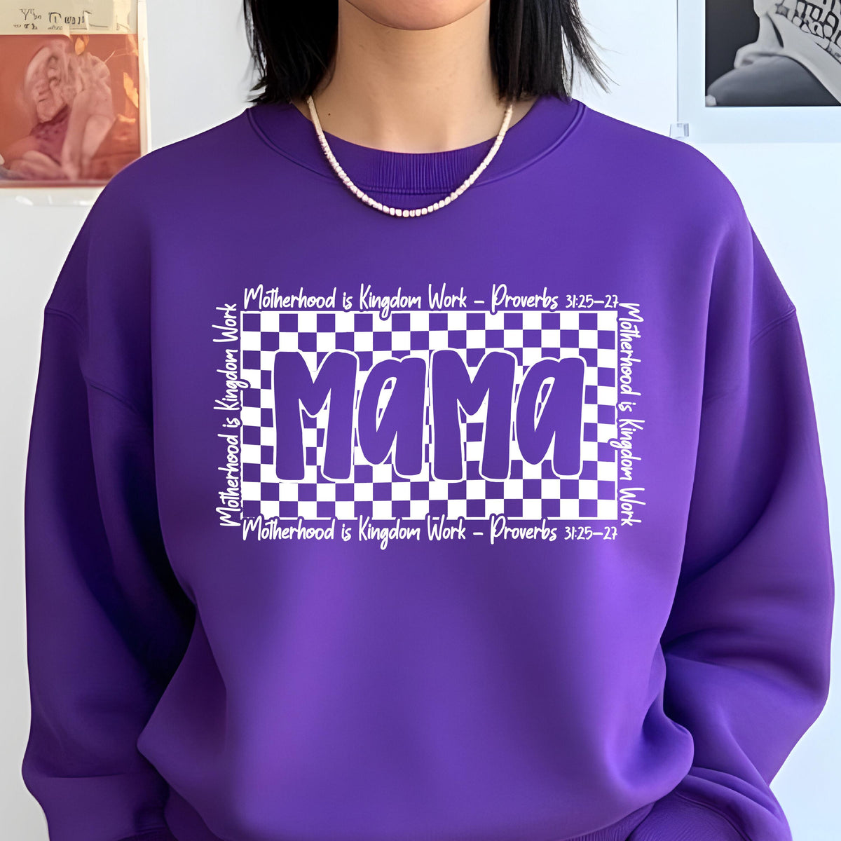 May include: Purple sweatshirt with a white checkered design and the word "Mama" in white letters. The text "Motherhood is Kingdom Work - Proverbs 3:25-27" is written on the top and bottom of the checkered design.