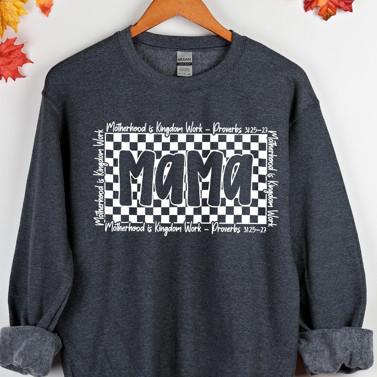 May include: A dark gray sweatshirt with a black and white checkered design and the word "Mama" in white letters. The text "Motherhood is Kingdom Work - Proverbs 3:25-27" is repeated around the checkered design.