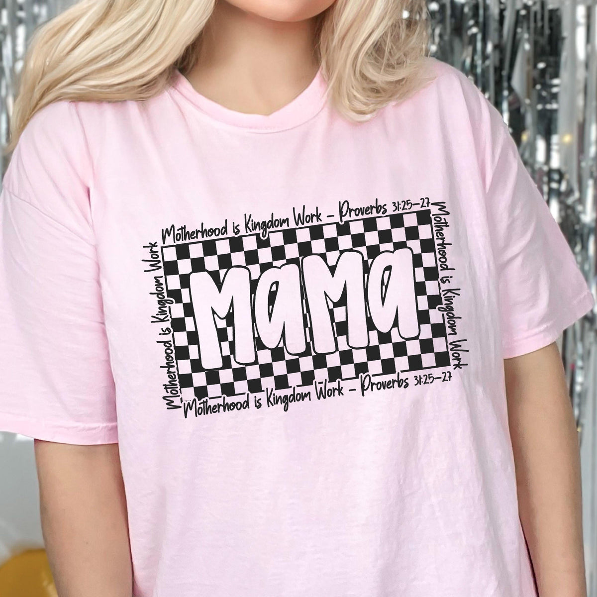 May include: Pink t-shirt with a black and white checkered design and the word "Mama" in white letters. The text "Motherhood is Kingdom Work - Proverbs 3:25-27" is written around the checkered design.