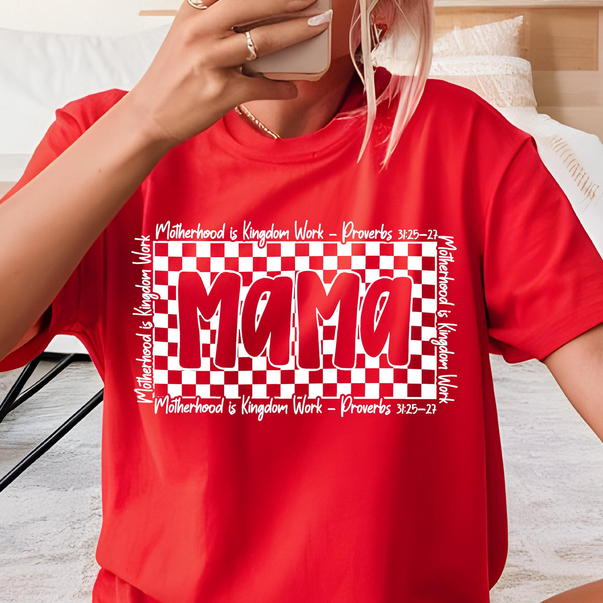 May include: Red t-shirt with a white checkered background and the word "Mama" in red letters. The text "Motherhood is Kingdom Work - Proverbs 3:25-27" is written on the top and bottom of the checkered background.