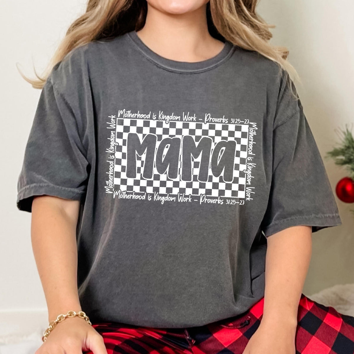 May include: A gray t-shirt with a black and white checkered design and the word "mama" in white lettering. The text "Motherhood is Kingdom Work - Proverbs 31:25-27" is written above and below the checkered design.