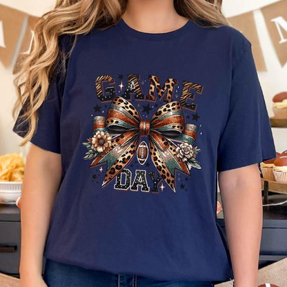 May include: A navy blue t-shirt with a graphic of a leopard print bow with a football in the center. The text "GAME DAY" is written in black letters above and below the bow.