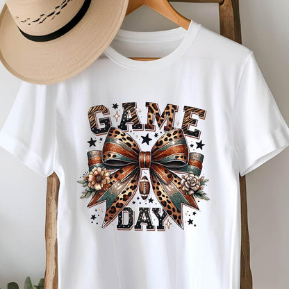 May include: White t-shirt with a graphic of a leopard print bow with a football and the text "GAME DAY" in black and gold letters.