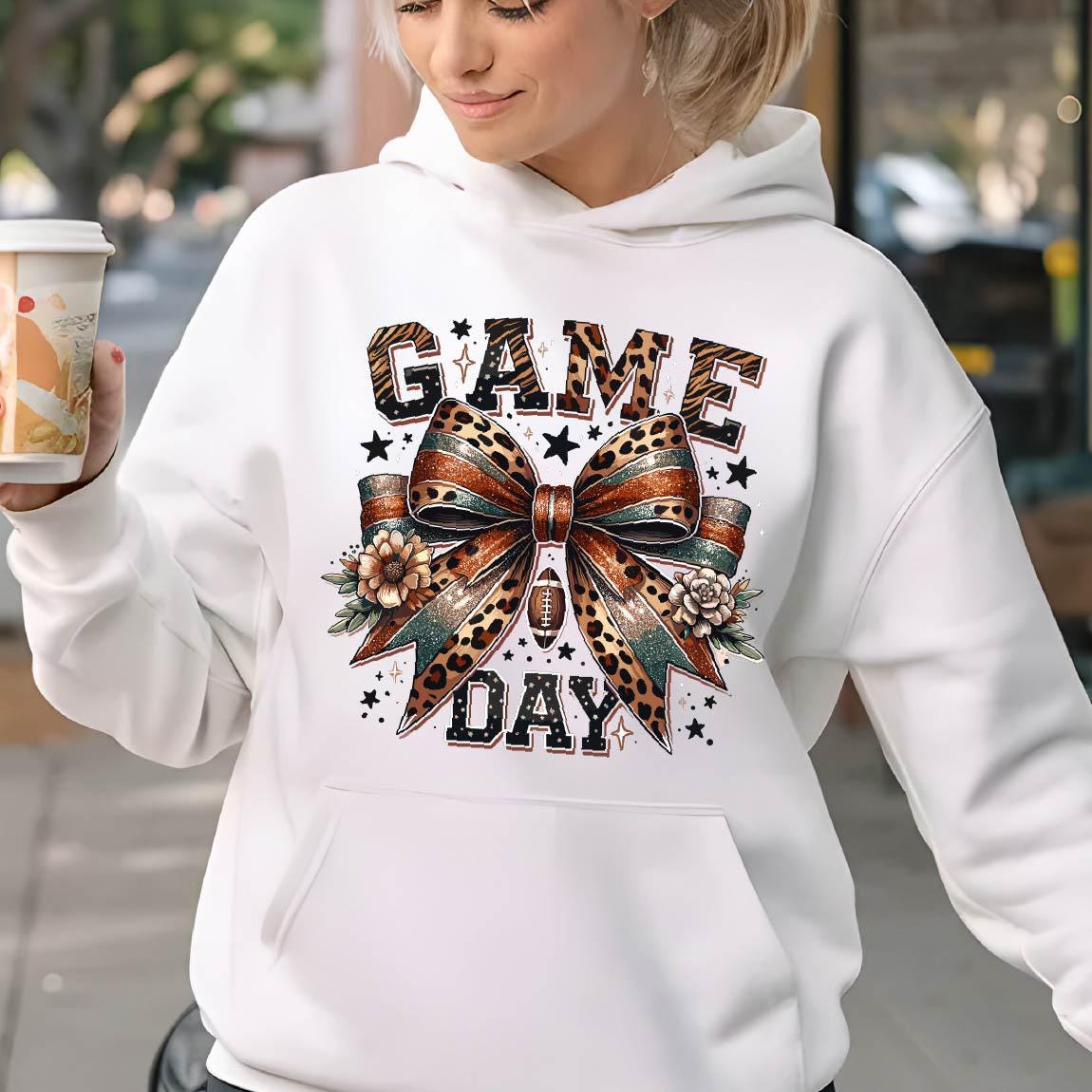 May include: White hoodie with a graphic print of a leopard print bow with a football and the text "GAME DAY" in black letters.