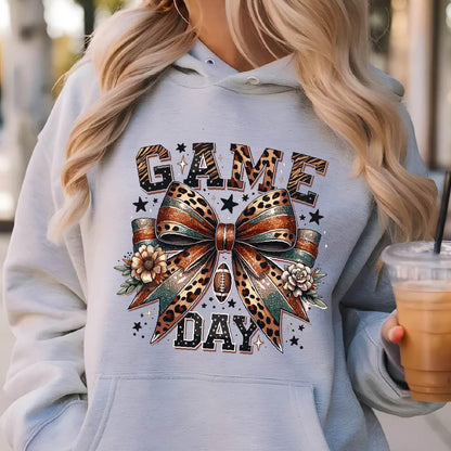 May include: A gray hoodie with a graphic of a leopard print bow with glitter and the words "GAME DAY" in black and brown letters.
