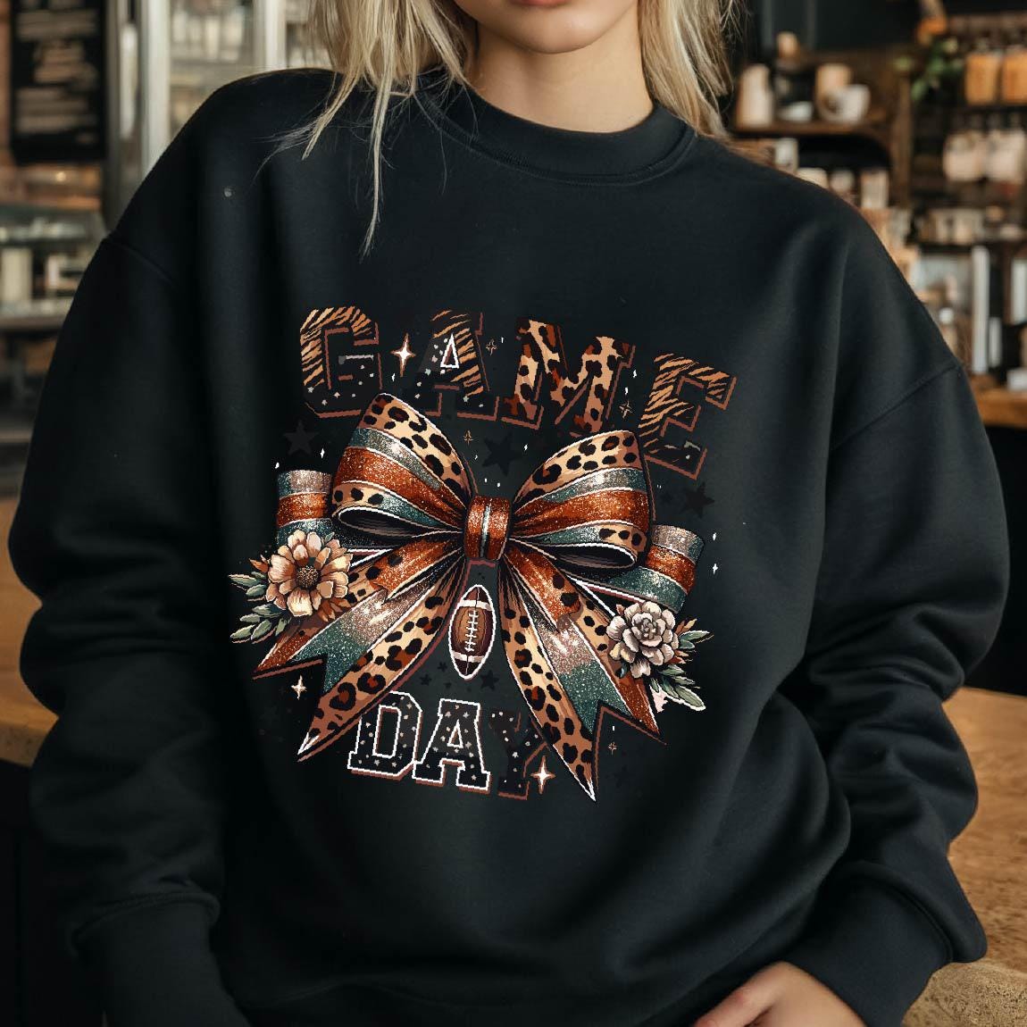 May include: Black sweatshirt with a graphic print of a leopard print bow with a football in the center. The text "GAME DAY" is printed below the bow.
