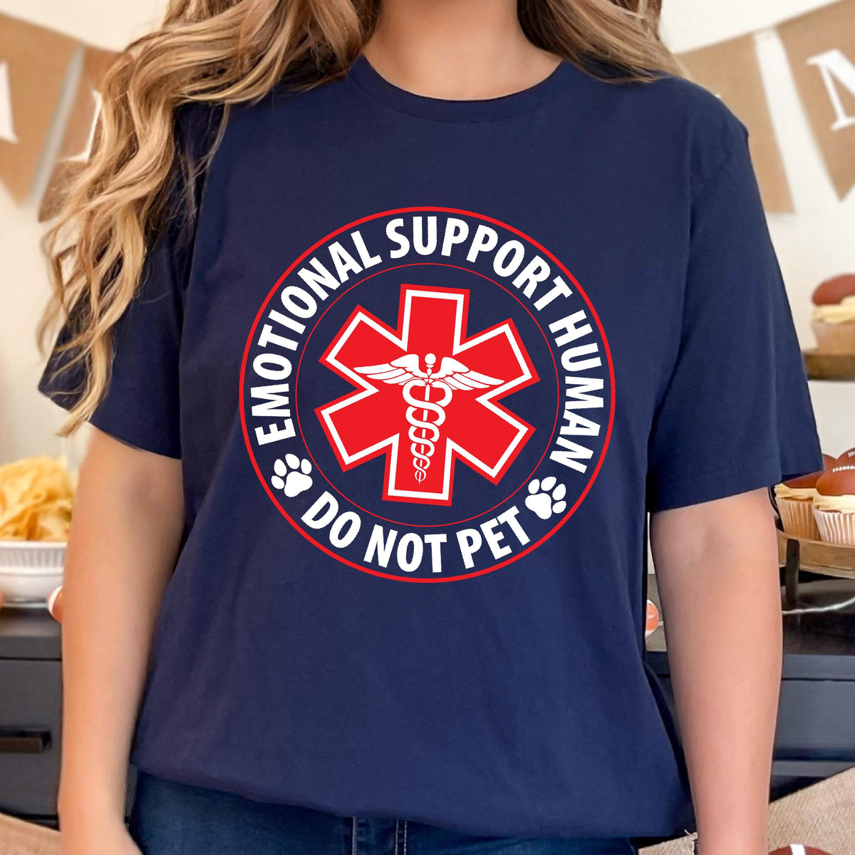 May include: Navy blue t-shirt with a red and white graphic. The graphic features a red star of life symbol with a caduceus in the center, surrounded by the words "EMOTIONAL SUPPORT HUMAN" and "DO NOT PET".